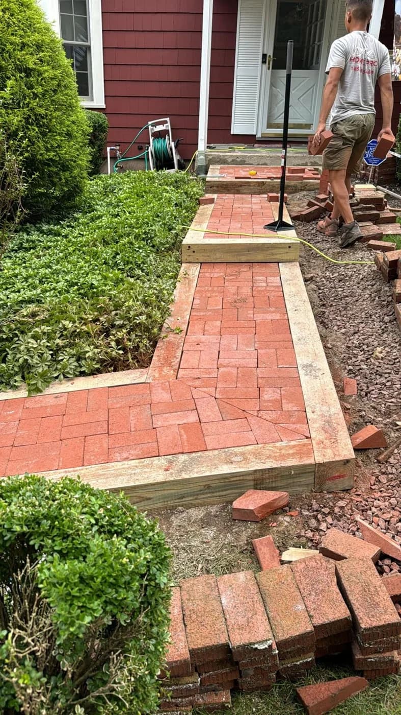 Home Pro worker beside the red brick walkway with timber borders during masonry work