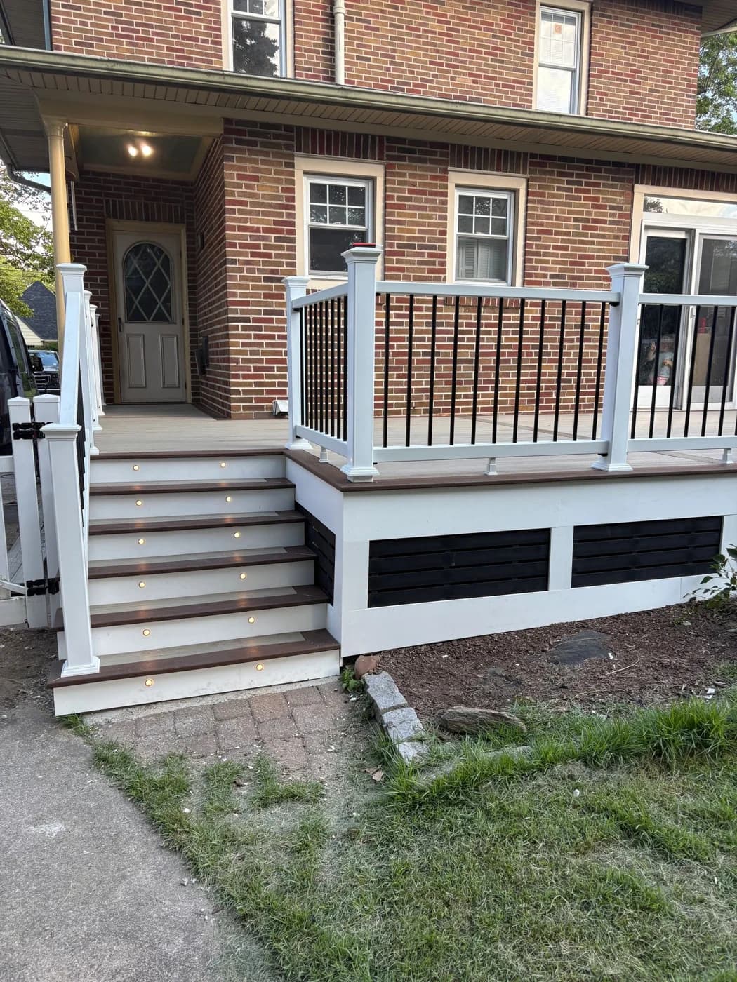 Side view of the same brick-home deck and white-railed staircase