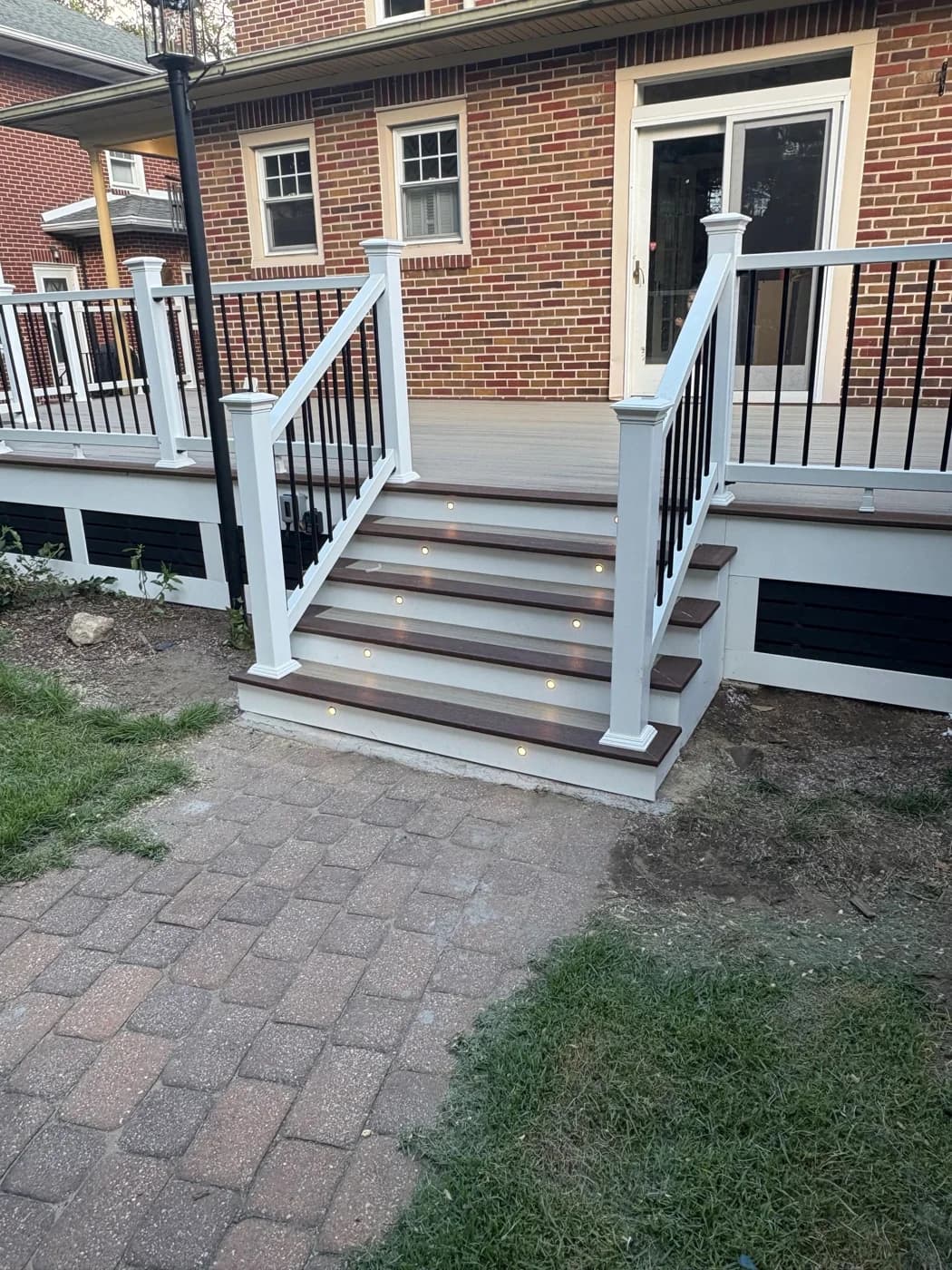 Stairs from the same brick-home deck, with white railings and recessed riser lights