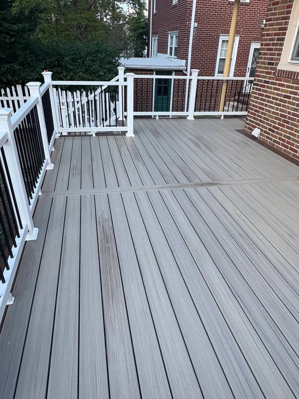 Gray deck beside a red-brick home with white rails and black balusters