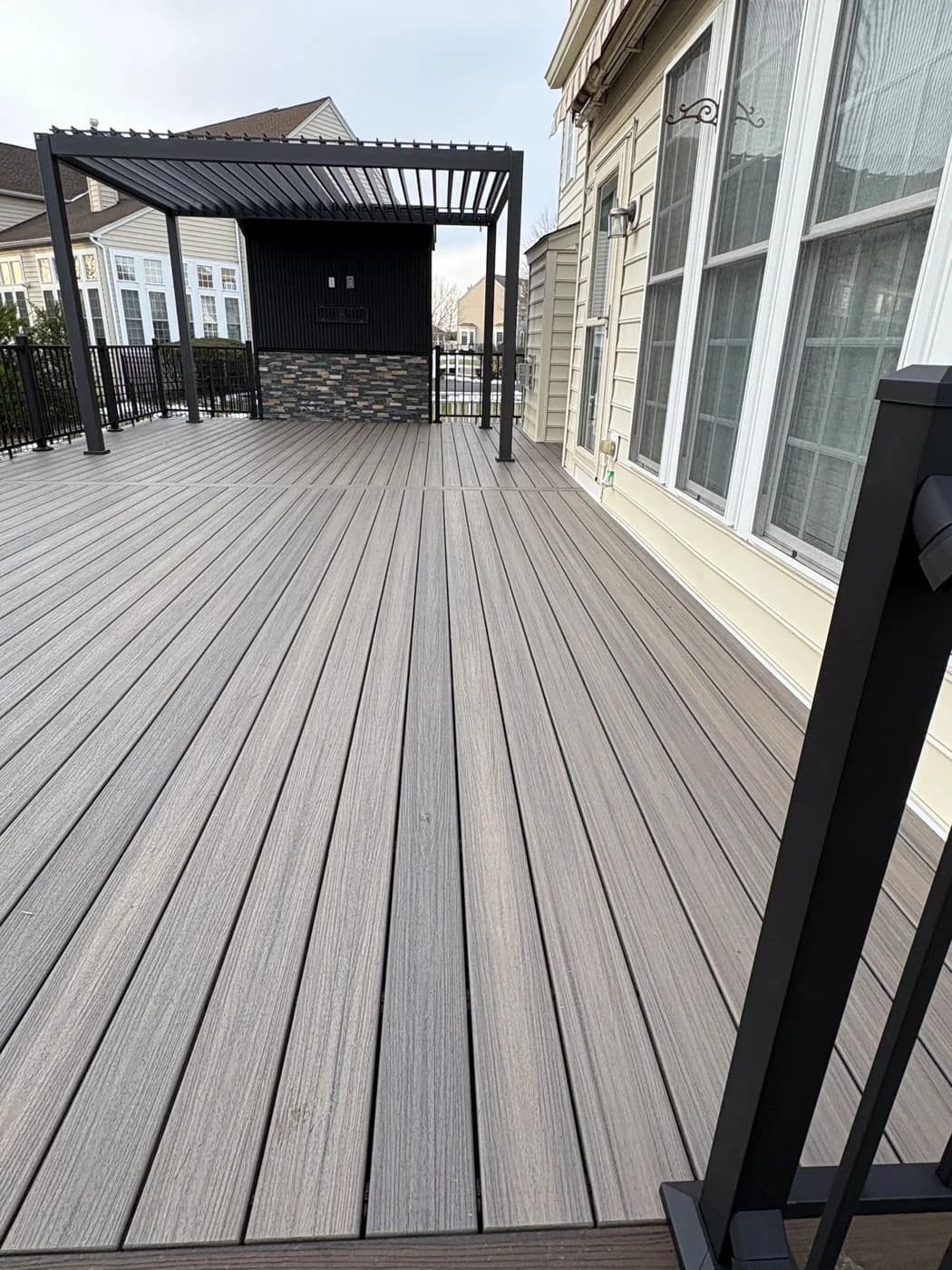 Gray deck boards beneath the black pergola beside its stone accent wall
