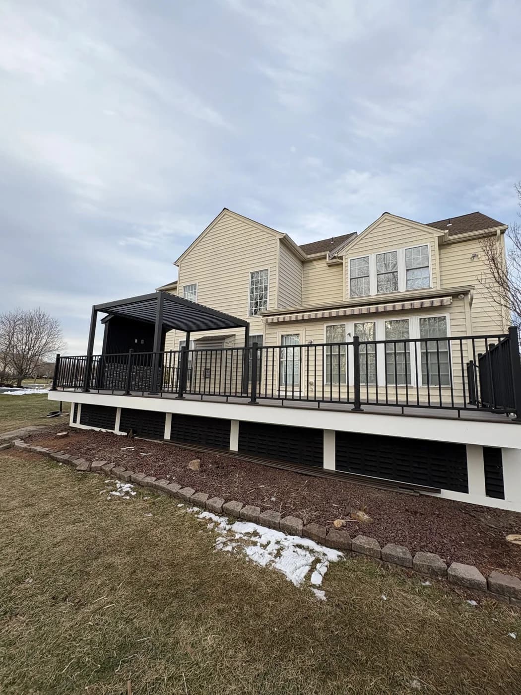 Wide view of the gray deck with black railings and pergola beside a beige home