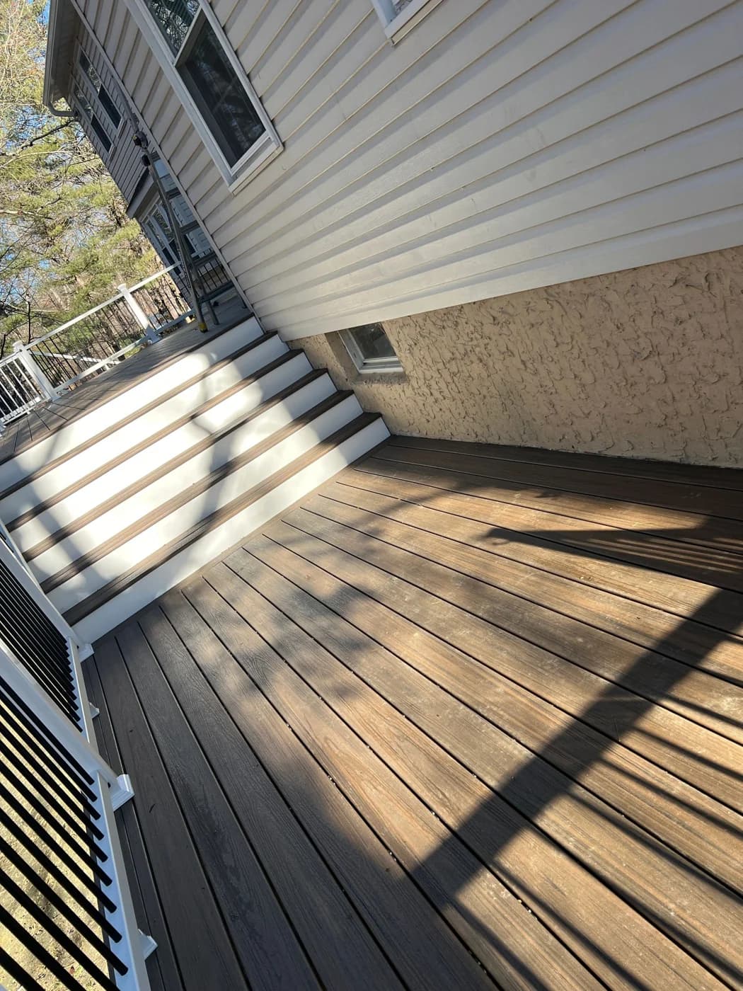 Deck beside beige siding with white-railed stairs and a tan foundation