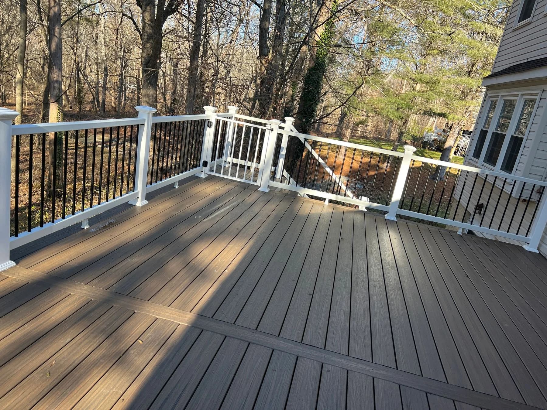 Upper deck corner with white posts and black balusters facing the trees