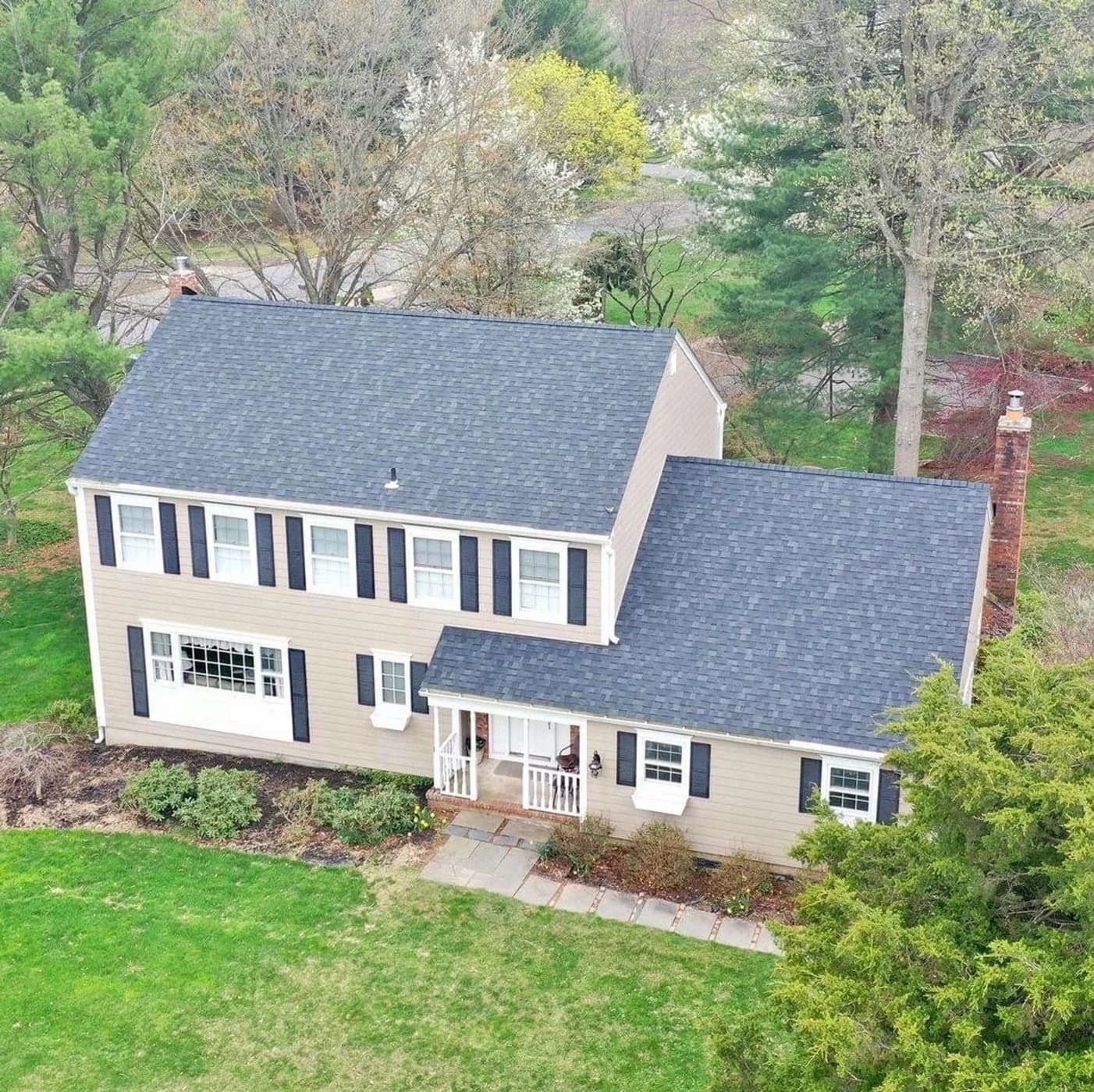 Beige colonial home with a dark shingle roof and black shutters
