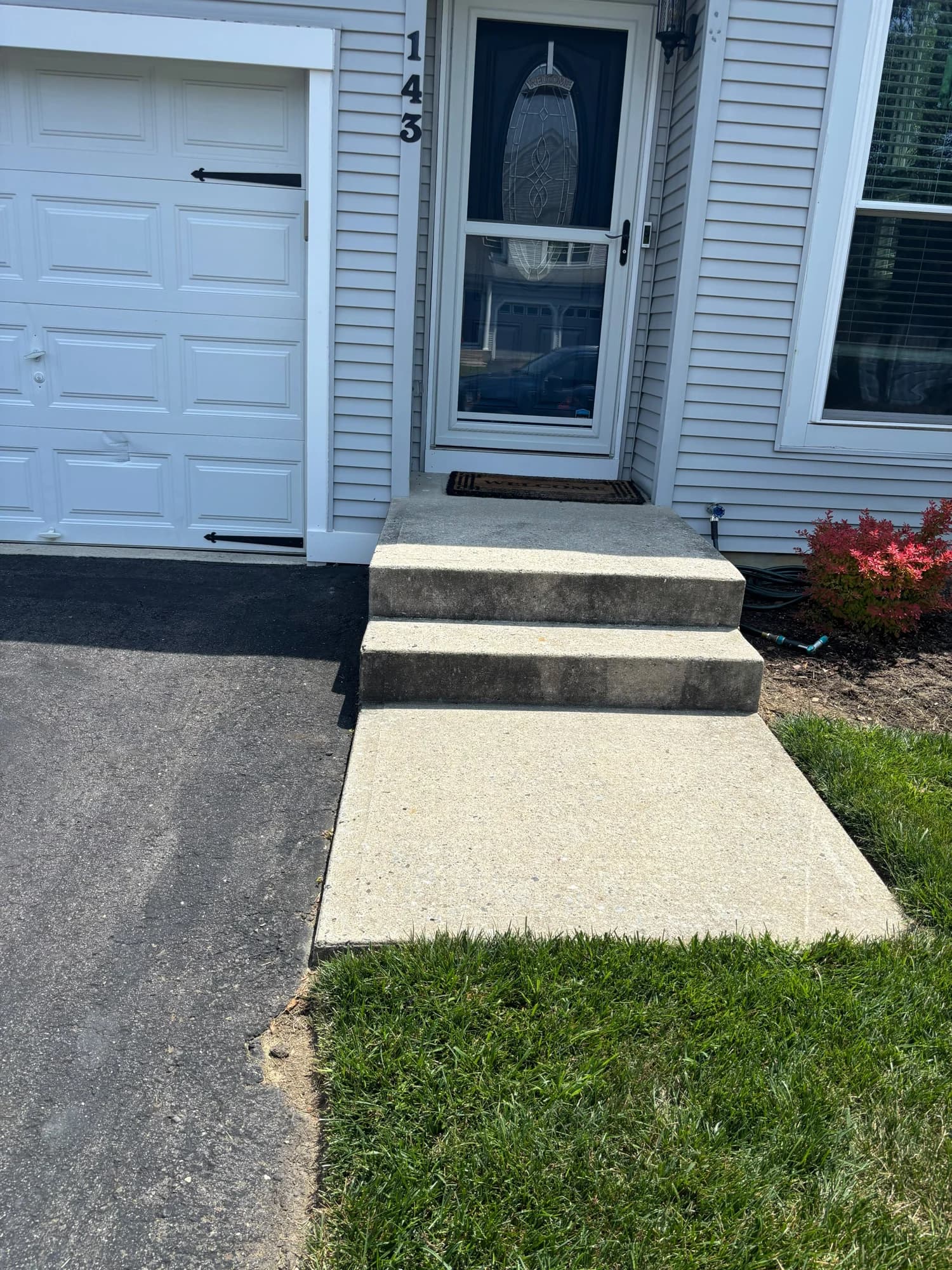 Concrete entry steps and doorway landing beside the garage and front lawn