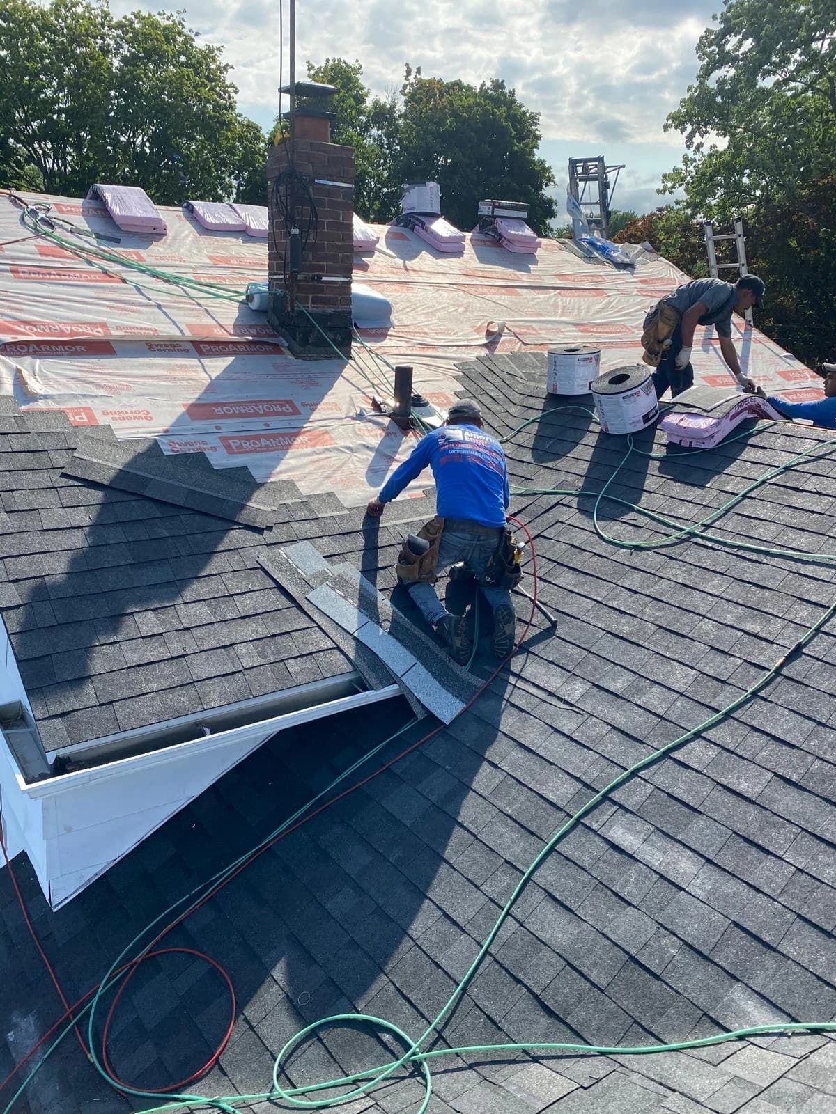Roofing crew laying gray shingles beside exposed printed underlayment