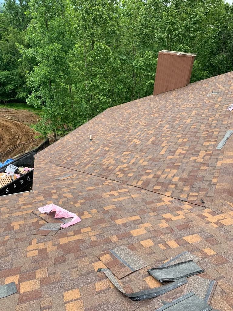 Brown and gold dimensional shingles beside a chimney and roof vent during installation