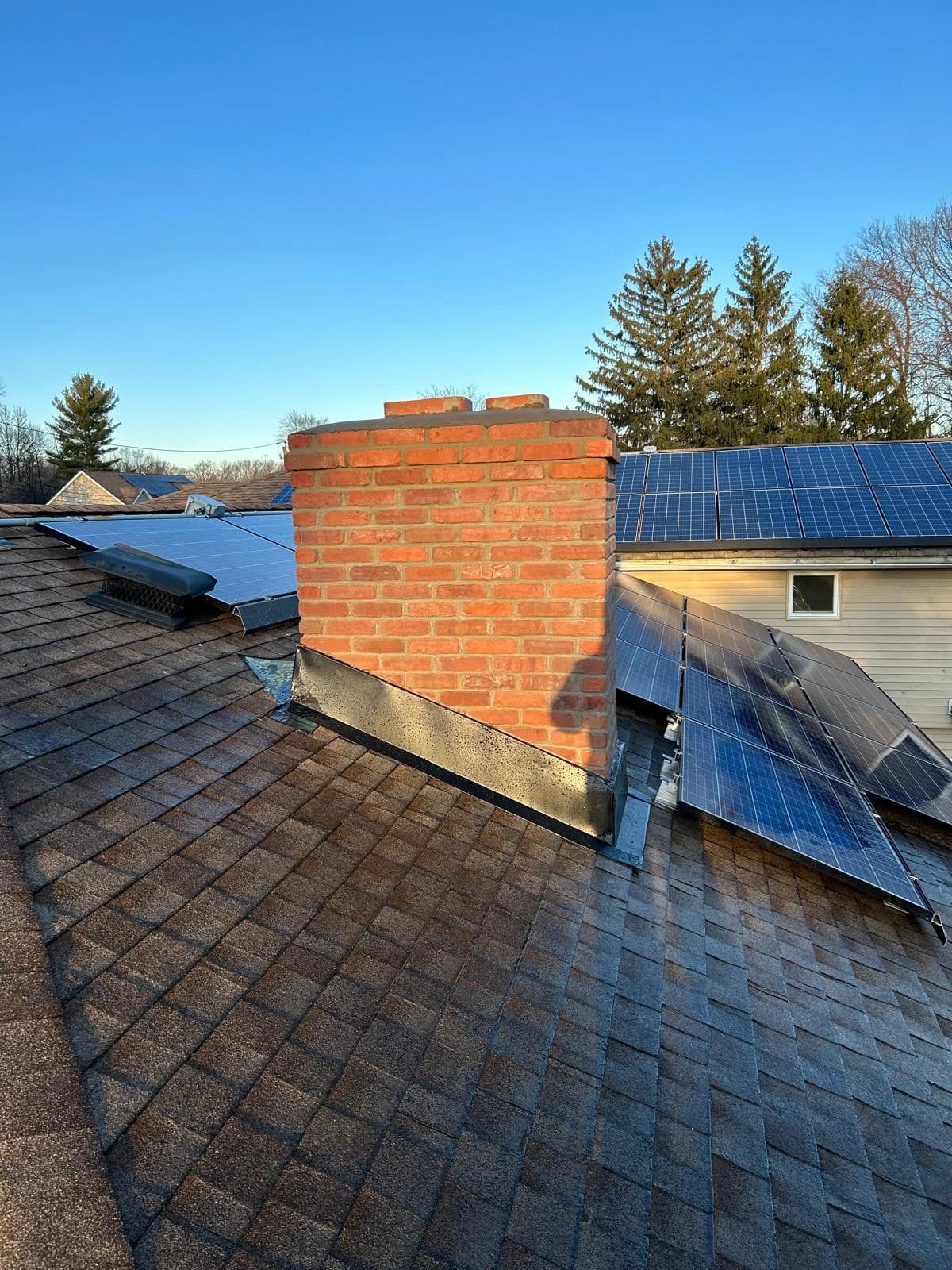 Close view of red-brick chimney masonry and dark flashing beside solar panels