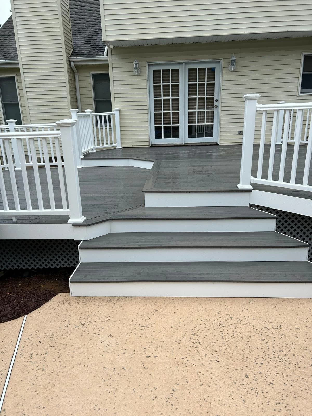 Broad gray steps, angled landing and white railings meeting the lower patio