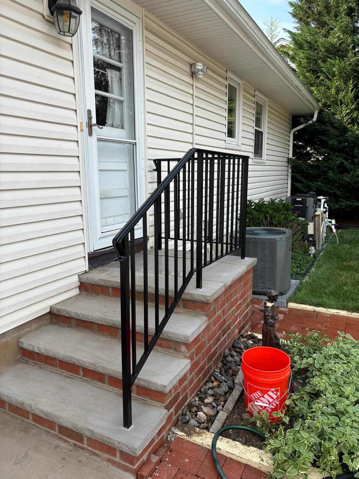 Brick side-entry staircase with gray treads and black metal railings beside white siding